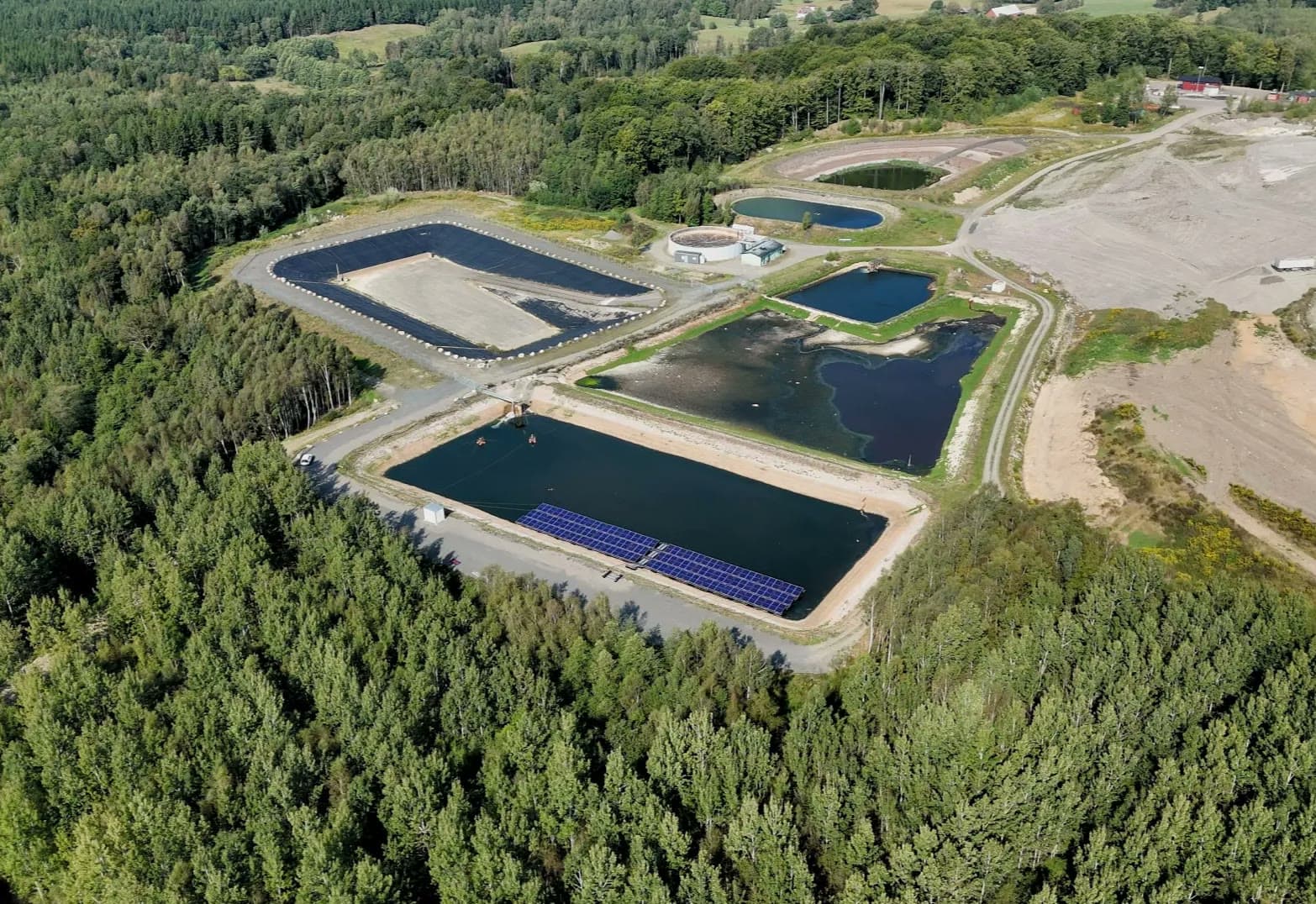 Flytande solpark i en lakvattendamm omgiven av skog, sett från luften