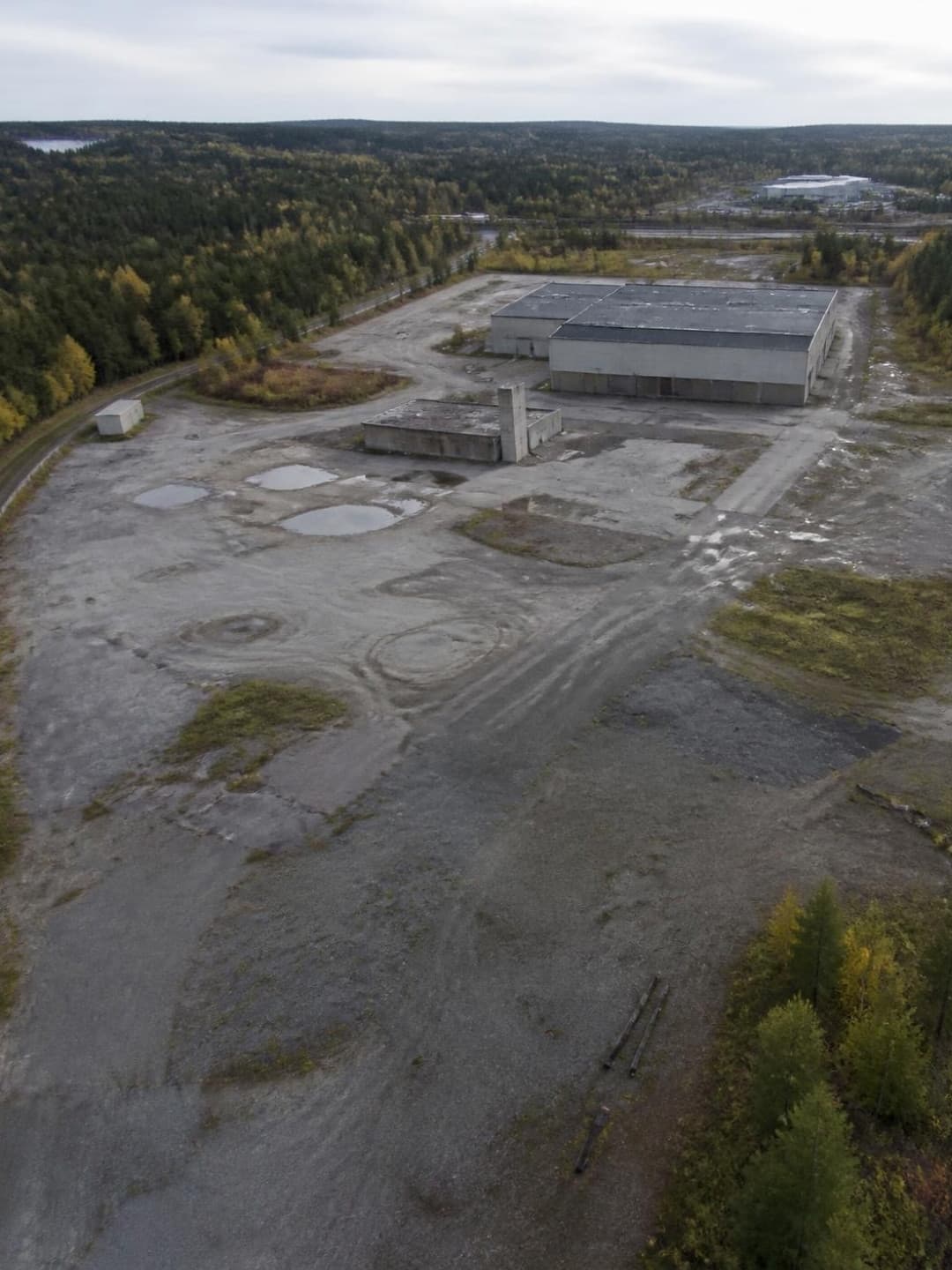 Grus- och asfaltsyta med lagerbyggnader vid en skogskant