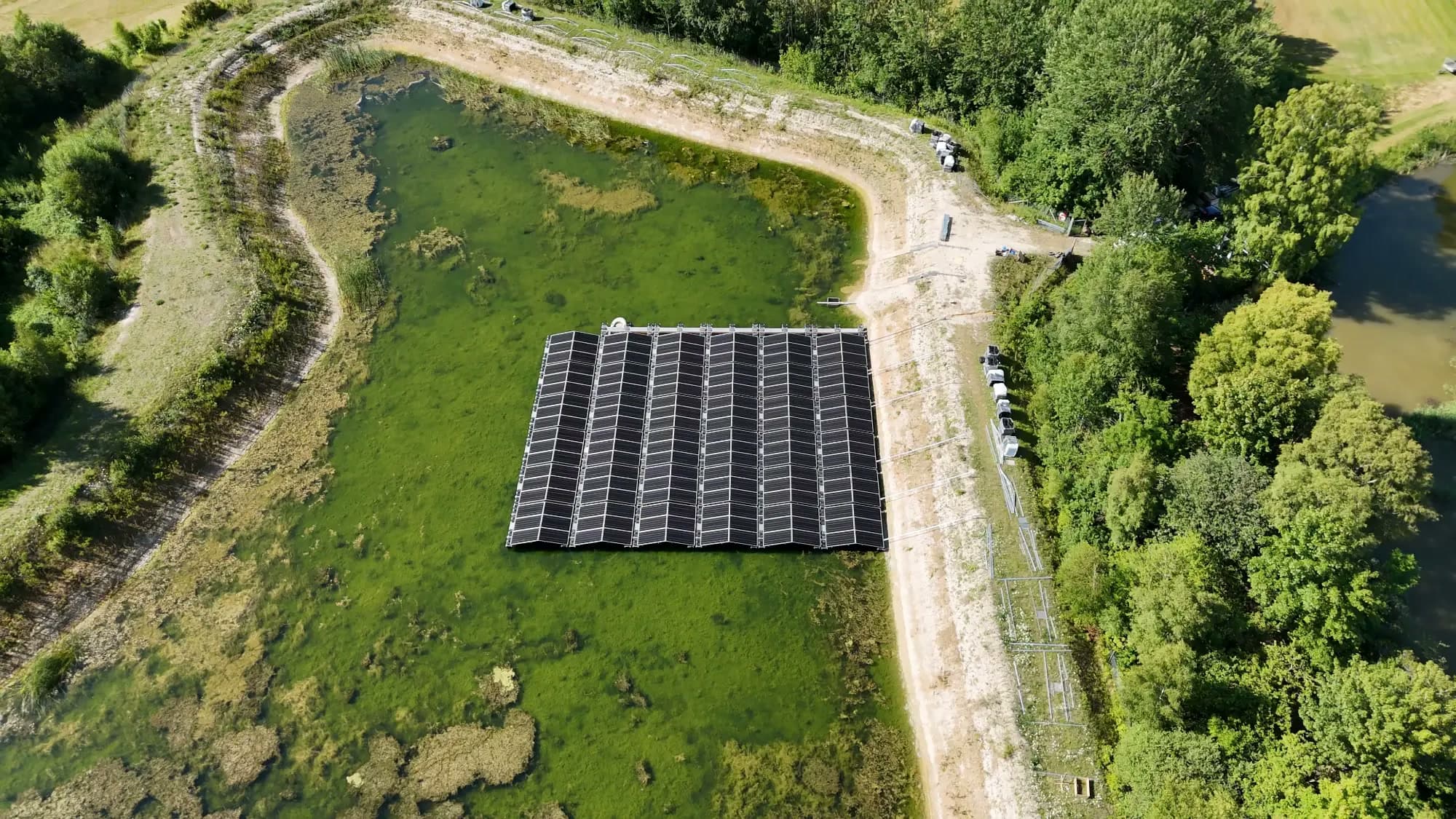 Flytande solpark med PowerModule i en grön damm omgiven av träd, sett från luften