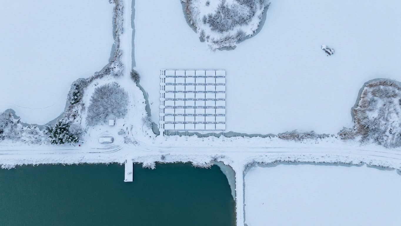 Snötäckt flytande solpark i en frusen damm, sett rakt ovanifrån