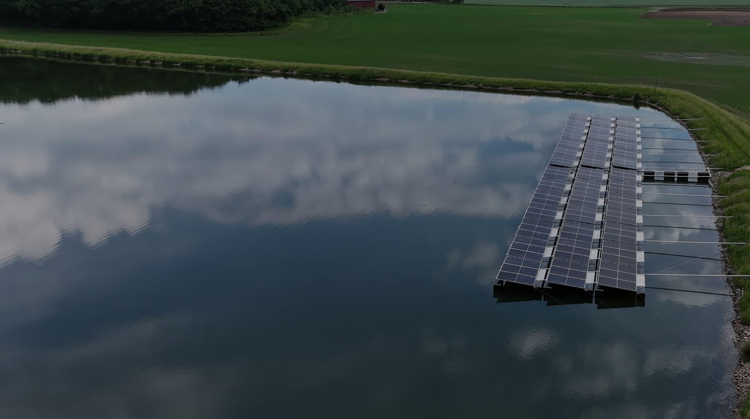Flytande solpark i en damm där molnen speglar sig i vattnet, sett från luften