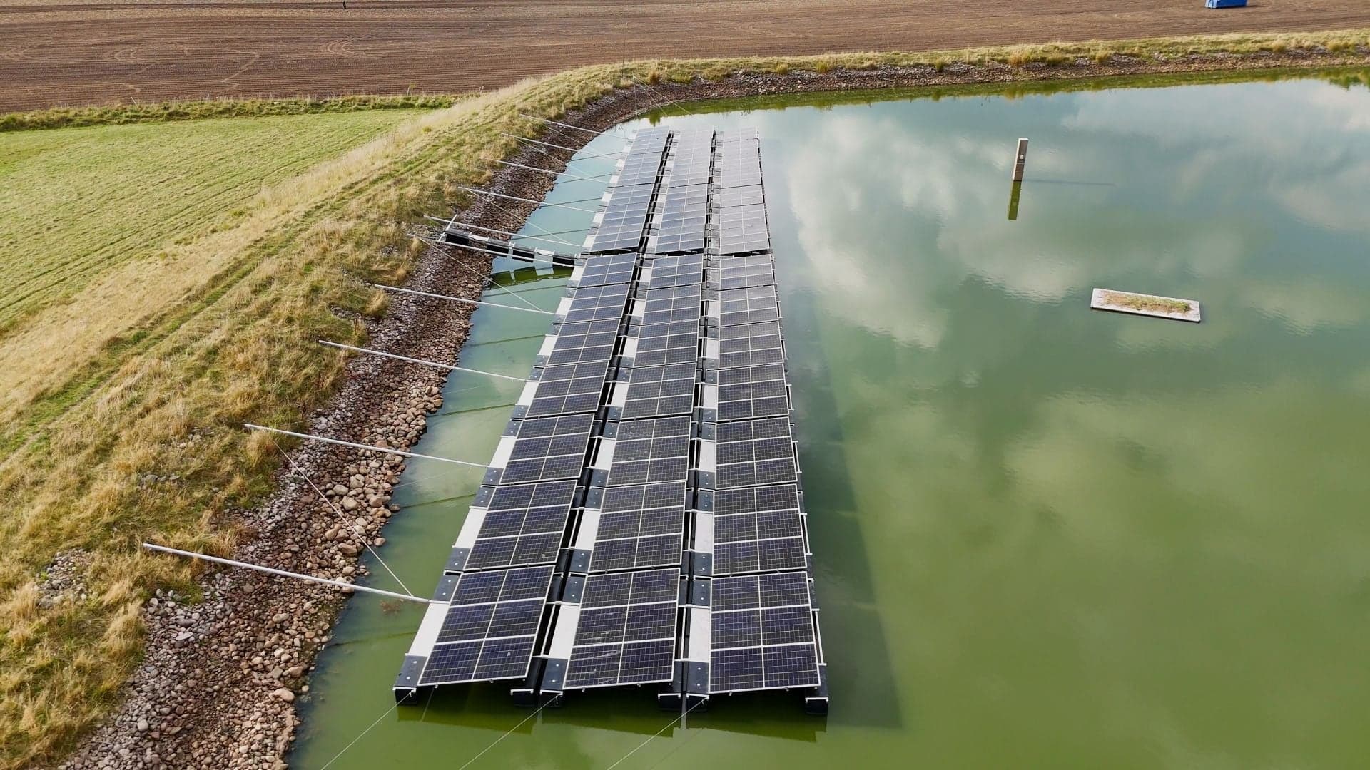 Flytande solpark på en damm mellan åkrar, sett från luften